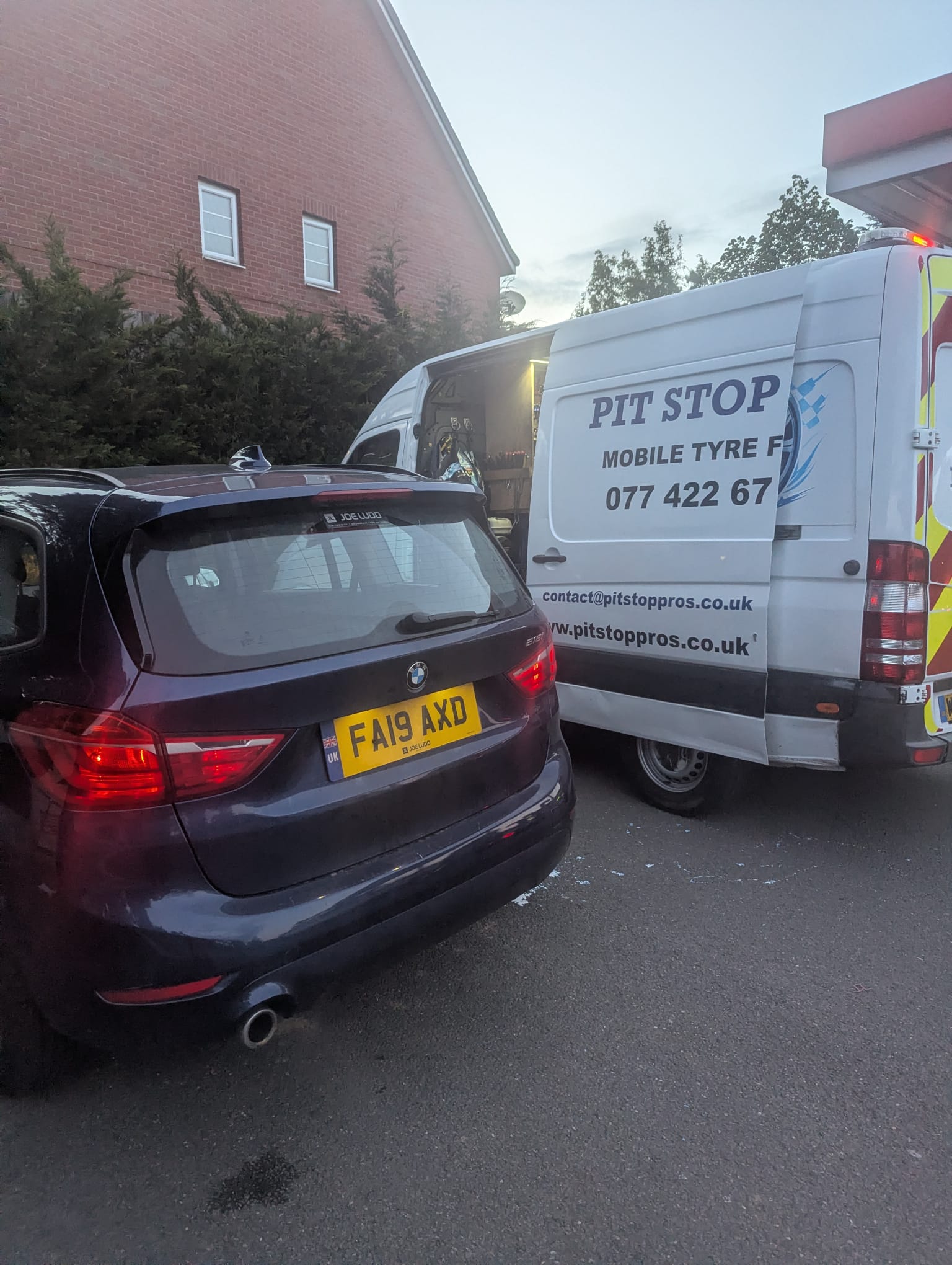 Van parked at dusk servicing a sedan on a roadside